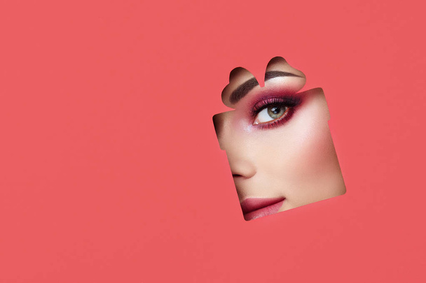 Face of a Young Beautiful Woman with a Beauty Make-up. Extension Eyelashes, Beautiful Green Eyes with Pink Shadows. Gift Box. Christmas Patterns. Red Paper - Foto, Imagen