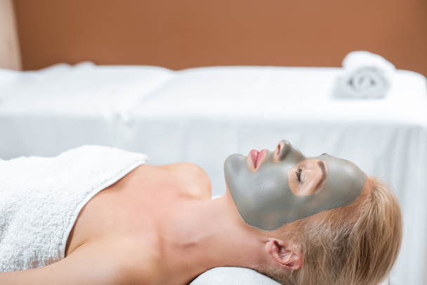 beautiful blonde woman lying with facial clay mask in spa  - Photo, Image