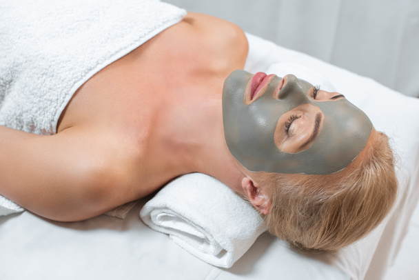 close up de mulher deitada com os olhos fechados e máscara de barro facial no spa
 - Foto, Imagem