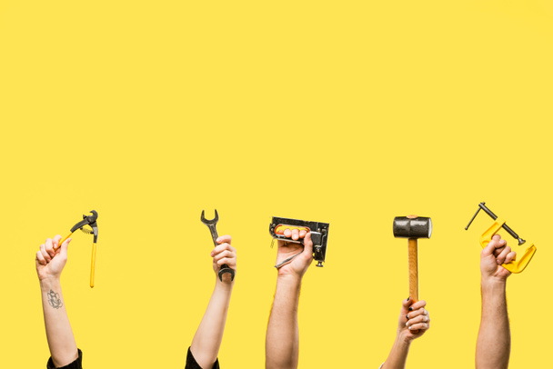 Cropped shot of hands holding staple gun, wrench, handheld, hammer isolated on yellow - Foto, Imagen