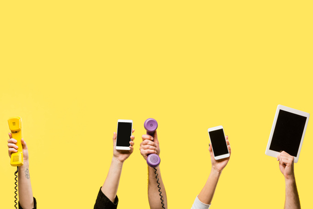 περικοπεί shot από χέρια που κρατούν smartphones, ψηφιακό tablet και τηλέφωνα που απομονώνονται σε κίτρινο  - Φωτογραφία, εικόνα