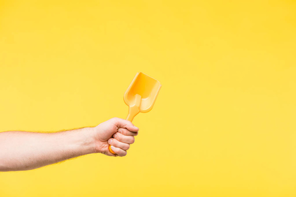 cropped shot of person holding toy shovel isolated on yellow - Fotó, kép
