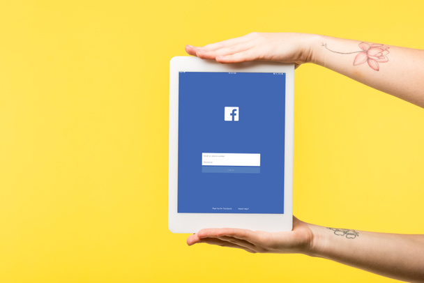cropped shot of person holding digital tablet with facebook app isolated on yellow  - Foto, Imagem