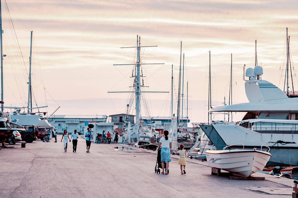 People stroll along the pier. Yacht bay on amazing backgrount with city and mountains at sunset. - Foto, immagini