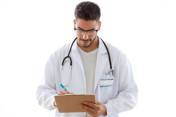 Shot of attractive young male doctor with stethoscope over neck taking notes in clipboard isolated on white background.  - 写真・画像