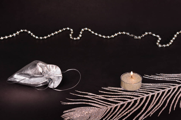 Decorações de Natal em fundo preto. Vela, saco de presente cordão de prata, pena e contas
 - Foto, Imagem