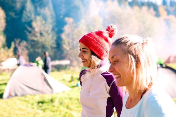 Kaksi naista leirintäalueella. Ystävät matkustavat yhdessä. Tytöt seisovat lähellä telttaa. Musiikkifestivaali ulkona. Telttailu vihreällä niityllä
. - Valokuva, kuva