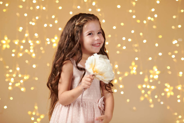 παιδί κορίτσι είναι σε κίτρινο φόντο, Χριστουγεννιάτικα φώτα, ροζ φόρεμα - Φωτογραφία, εικόνα