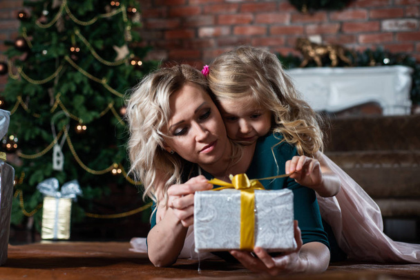 Mom and daughter looking at gift boxes on the background of a Christmas tree, lying on the floor - Fotó, kép