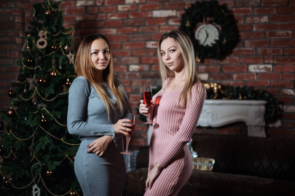 Two pretty young girlfriends or sisters celebrate Christmas together at home with champagne in hand - Foto, Imagen
