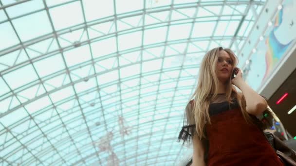 A beautiful girl descends the escalator and talks on the phone in the mall. - Filmagem, Vídeo