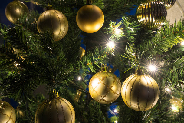 Detailní pohled na vánoční stromek se zlatými ornamenty a jasných zářivých světel v noci - Fotografie, Obrázek