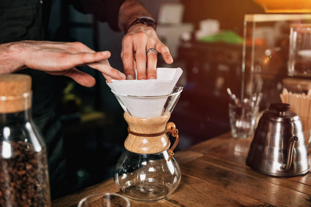 Close-up beeld van barista handen maken van filterkoffie. Barista met getatoeëerde armen dragen van donkere uniform.    - Foto, afbeelding