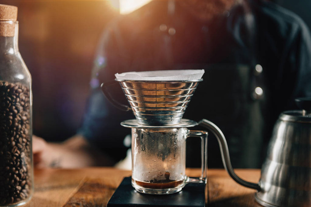 Close up Kalita Wave Dripper on black digital scale, wooden table. Tools and equipment for making Drip Brew coffee. Barista with tattooed arms wearing dark uniform.     - Foto, Imagem