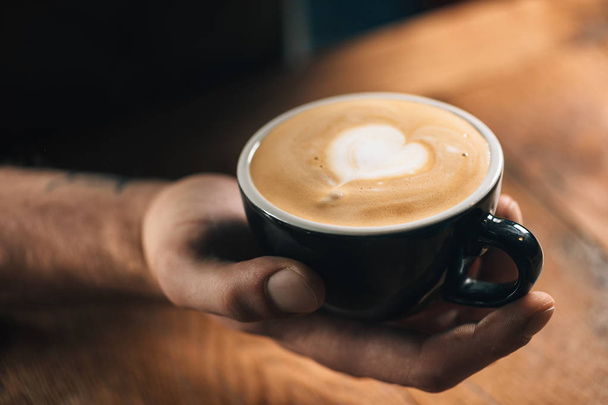 Professionele barista houdt van zwarte koffie beker met hart latte art oppervlak.  - Foto, afbeelding