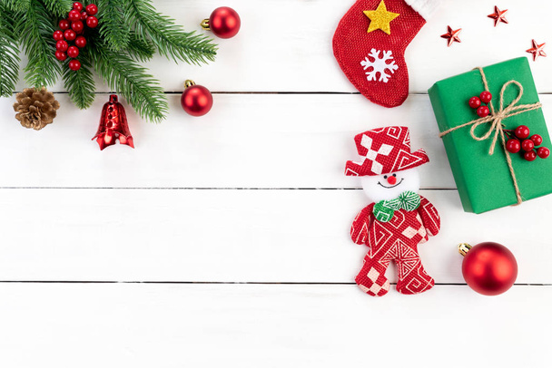 Концепция Рождества. Вид сверху на рождественскую зеленую подарочную коробку со снеговиком, ветками, сосновыми шишками, красными ягодами и колокольчиком на белом деревянном фоне
. - Фото, изображение