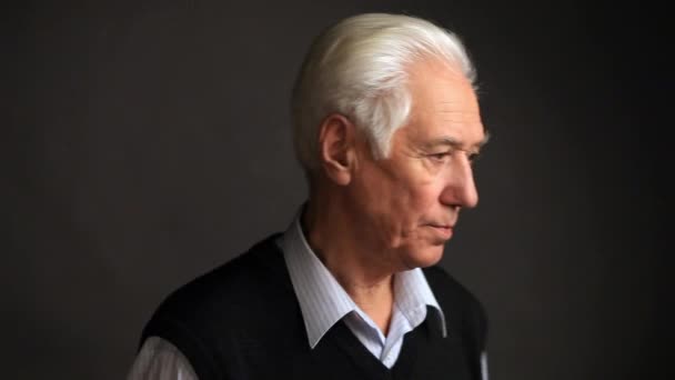 Uomo anziano dai capelli grigi con le mani incrociate guarda attentamente la fotocamera, sfondo grigio studio
 - Filmati, video