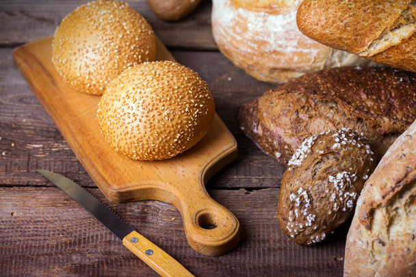 different fresh bread and buns on the wooden tabl - Foto, Imagen