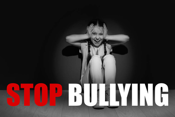 Message STOP BULLYING and crying little girl sitting on floor near dark wall, black-white effect - Foto, immagini