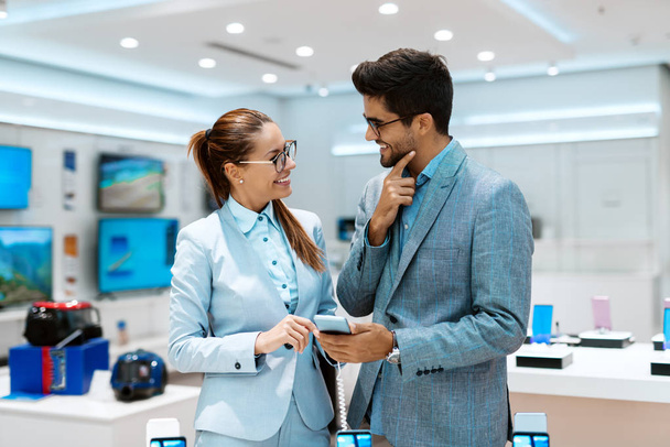 Szczęśliwa para ubrany w odzież firmy, wybierając nowy inteligentny telefon stojąc w sklepie tech. - Zdjęcie, obraz