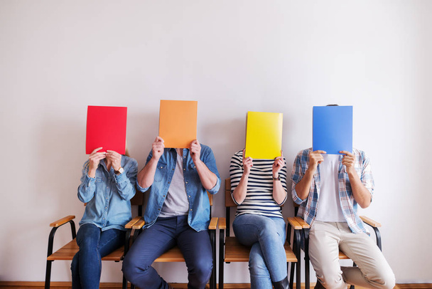 группа молодых людей, покрывающих лица красочными папками
  - Фото, изображение