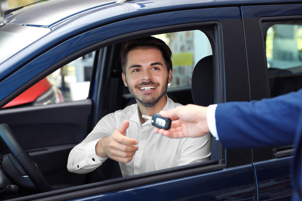 Young salesman giving car key to client in dealership - Zdjęcie, obraz