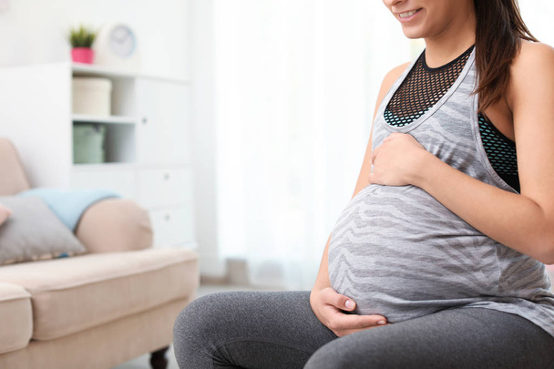 Young pregnant woman in fitness clothes at home, closeup. Space for text - Foto, afbeelding