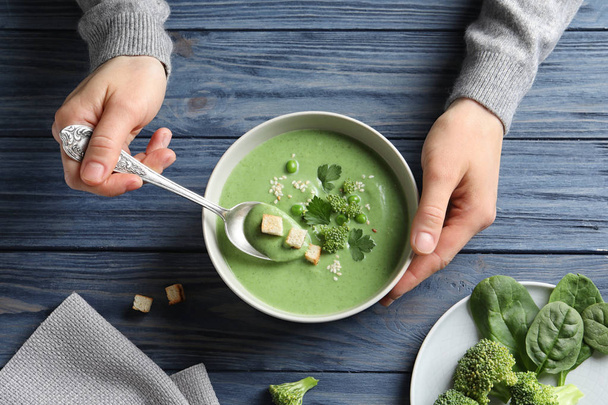 Woman eating fresh vegetable detox soup made of broccoli and green peas with croutons at table, top view - Фото, изображение