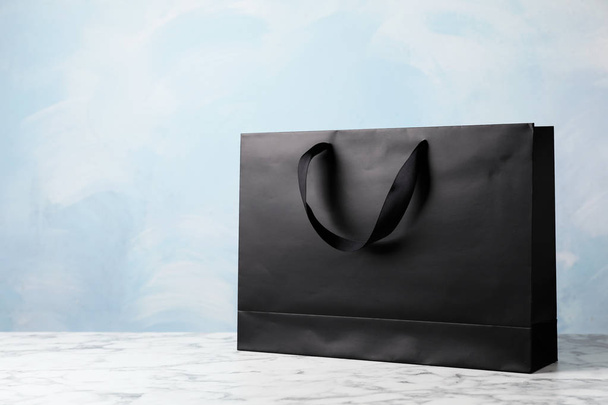 Paper shopping bag with ribbon handles on table against color background. Mockup for design - Foto, imagen