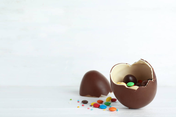 Cracked chocolate Easter egg with candies on table. Space for text - Valokuva, kuva