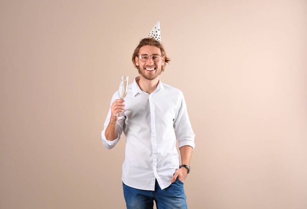 Portrait of happy man with party cap and champagne in glass on color background - Foto, afbeelding