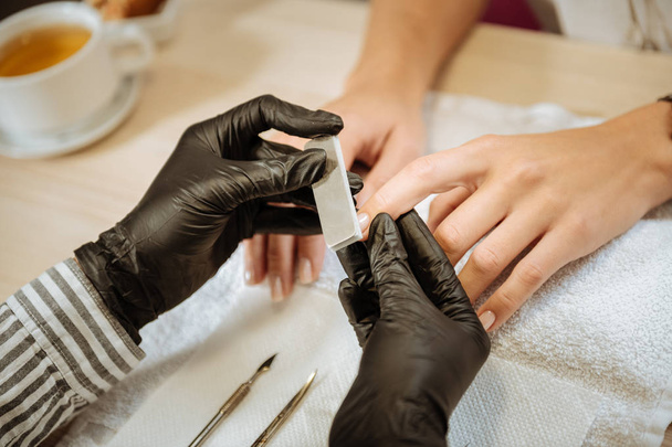 Instruments for manicure. Experienced nail artist wearing black gloves using instruments for manicure - Zdjęcie, obraz