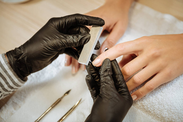 Top view of nail artist wearing black gloves polishing nails of her client - Zdjęcie, obraz