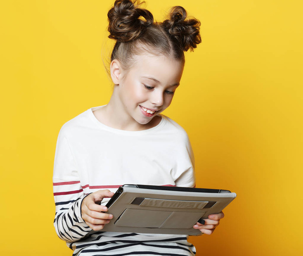Little girl with tablet on yellow studio background. - Photo, Image