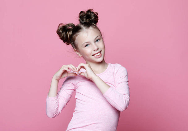 girl child over pink background smiling in love showing heart symbol and shape with hands. - Fotografie, Obrázek