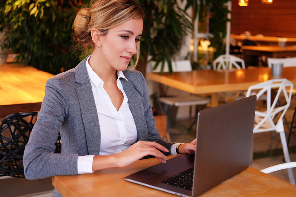 Wooman biznesowych za pomocą laptopa w kawiarni. Młoda piękna dziewczyna, siedząc w kawiarni i działa na komputerze. - Zdjęcie, obraz