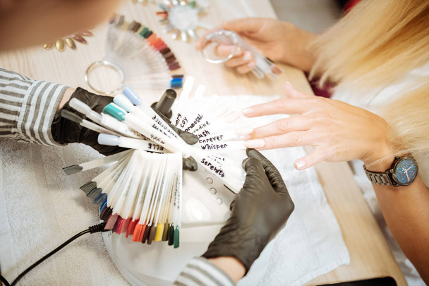 Experienced nail artist wearing black gloves choosing the best color - Φωτογραφία, εικόνα