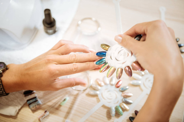 Vrouw denken over proberen helder blauwe of groene schellak voor nagels - Foto, afbeelding