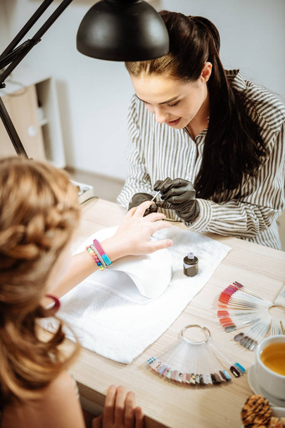 Dark-haired nail artist feeling busy making manicure for teenager - Фото, зображення