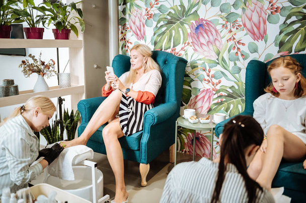 Blonde-haired businesswoman using her smartphone having pedicure - Foto, afbeelding
