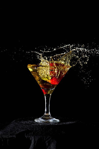 Yellow cocktail glass with a strawberry splashing. Black background. Frozen movement - Foto, Imagen