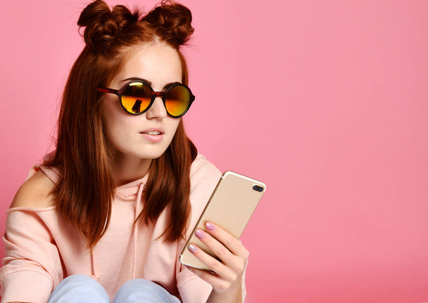 Serious young woman in trendy eyewear concentrated on information looking at phone - Foto, imagen