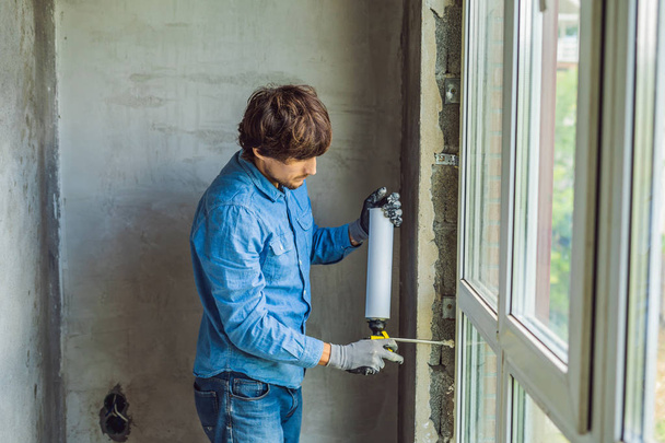 Man in casual blue shirt using mounting foam while window installation.  - Foto, Bild