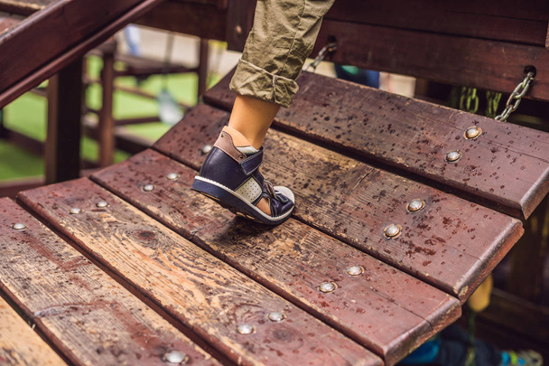 Leg on boy in orthopedic sandal on wooden bench outdoors. - Fotó, kép