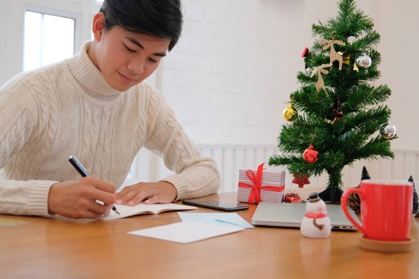 чоловік в кремовому светрі пише записку на блокноті вдома під час різдвяного новорічного святкування
. - Фото, зображення