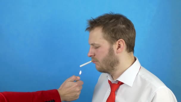 Parrakas mies valkoisessa paidassa ja solmiossa seisoo savukkeen kanssa, toinen mies sytyttää savukkeensa tuleen, työntää hänet tupakoimaan, nikotiinia, haittaa tupakoinnille, käsite
 - Materiaali, video
