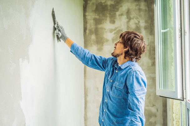 Male laborer applying white putty on wall and smearing by putty knife. - Fotoğraf, Görsel