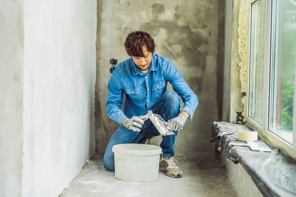 Young master mixing putty in bucket in room of renovating house in daytime. - Fotoğraf, Görsel