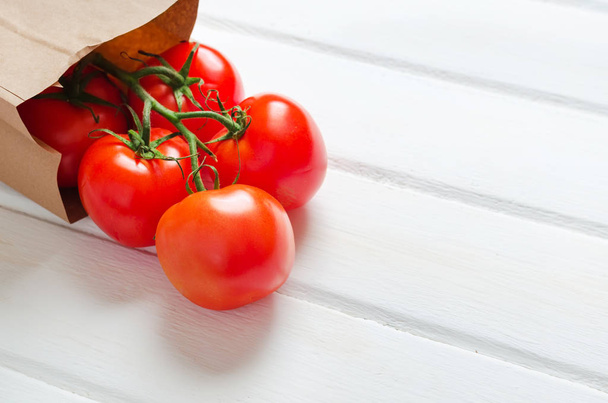 Tomato branch with paper bag on white wooden background. Copy space. Close up. - Foto, Imagen