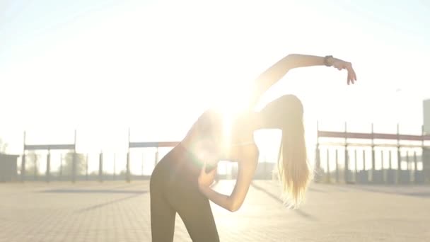 Silhouette of a fitness woman profile stretching at sunrise with the sun in the background. Healthy young woman warming up outdoors. She is stretching her arms and legs. - Кадри, відео